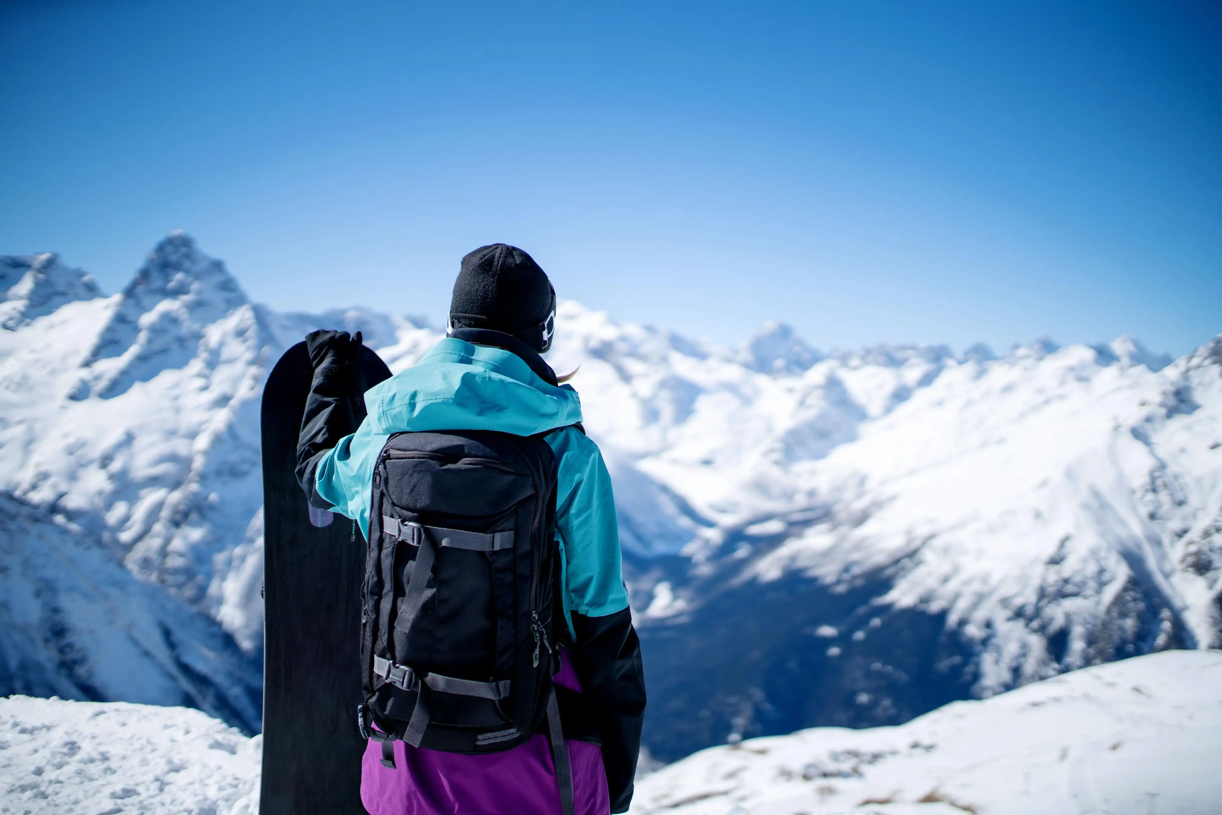 Woman holding snowboard while gazing at the white mountain in the background