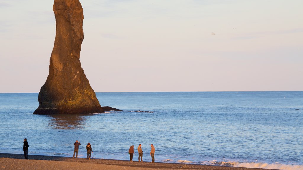 Reynisdrangar which includes a sunset and a sandy beach as well as a large group of people