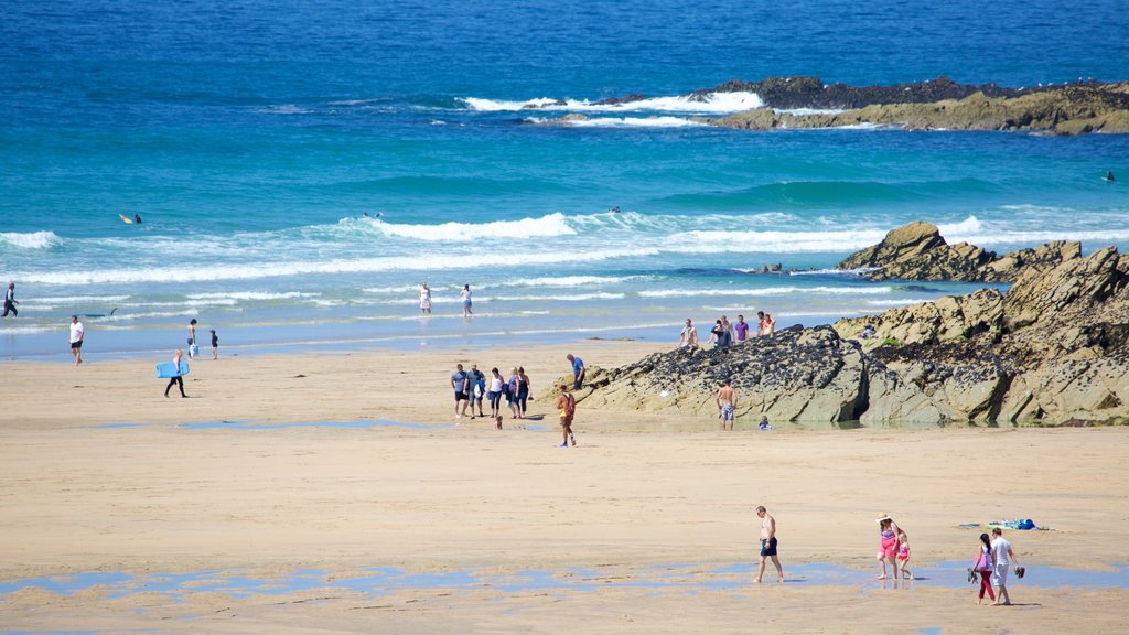 Fistral Beach mostrando litoral acidentado e uma praia de areia assim como um grande grupo de pessoas