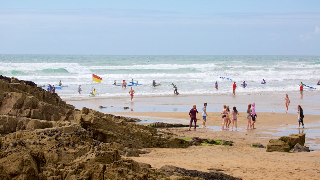 Bude Beach mostrando uma praia de areia e litoral rochoso assim como um pequeno grupo de pessoas