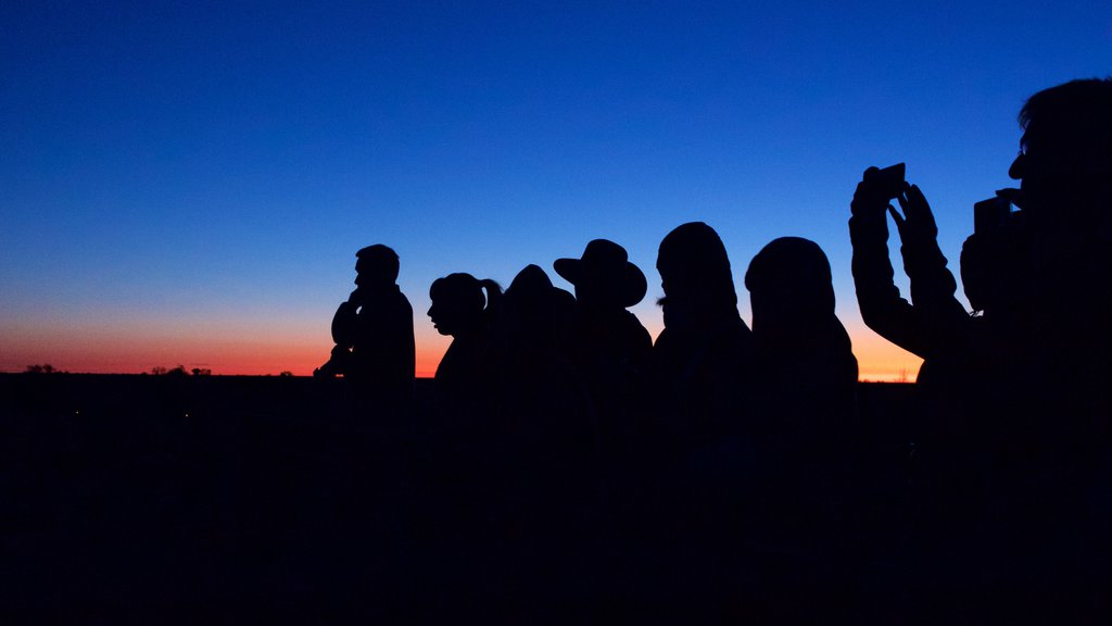 Uluru which includes a sunset and desert views as well as a small group of people