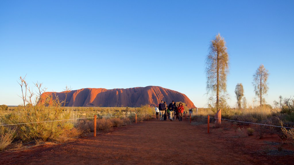 Uluru ofreciendo vistas de paisajes y vistas al desierto y también un pequeño grupo de personas