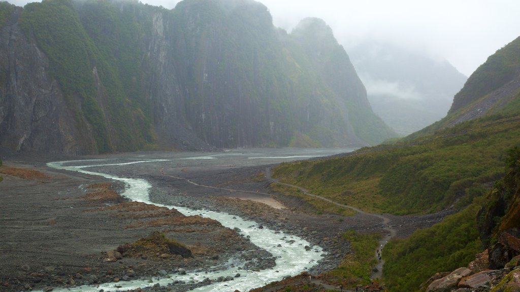 Foxglaciären som visar berg, dimma och en å eller flod