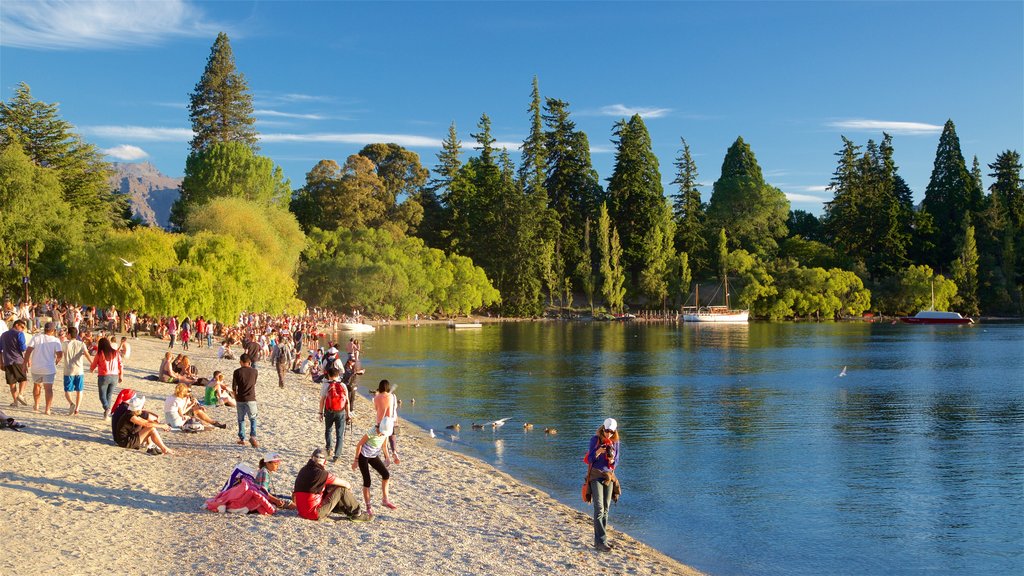 Playa de Queenstown que incluye una playa de piedras y un lago o espejo de agua y también un gran grupo de personas