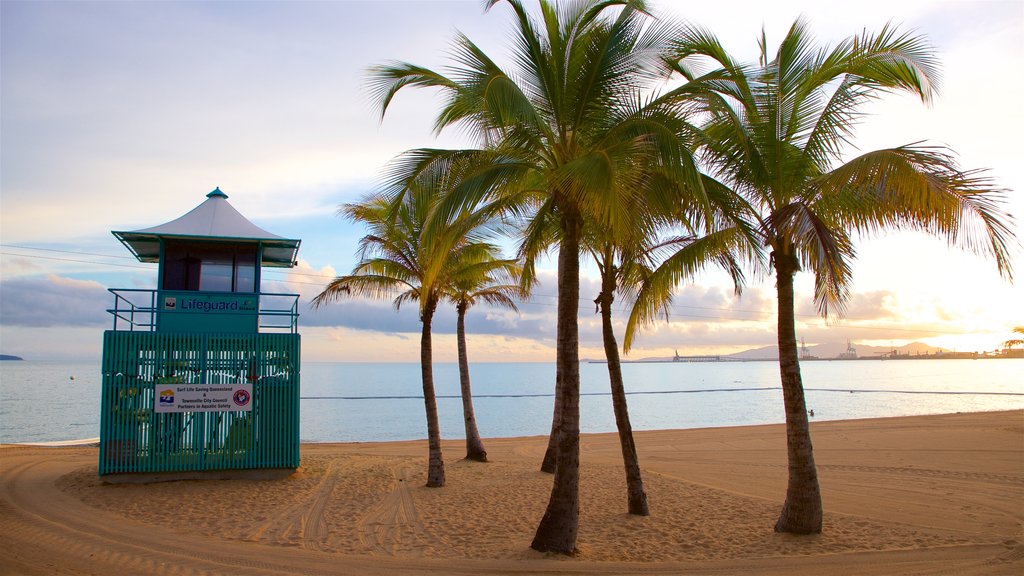 The Strand que incluye una playa de arena, escenas tropicales y una puesta de sol