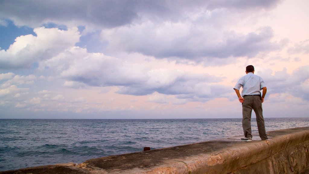 Malecón ofreciendo una puesta de sol y vistas generales de la costa y también un hombre