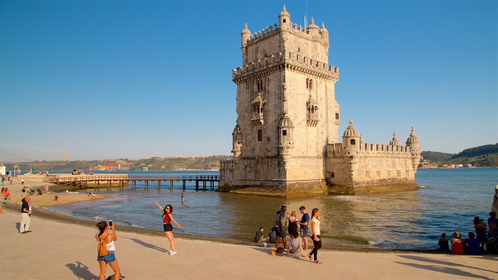 Torre de Belém mostrando arquitetura de patrimônio e um rio ou córrego assim como um pequeno grupo de pessoas