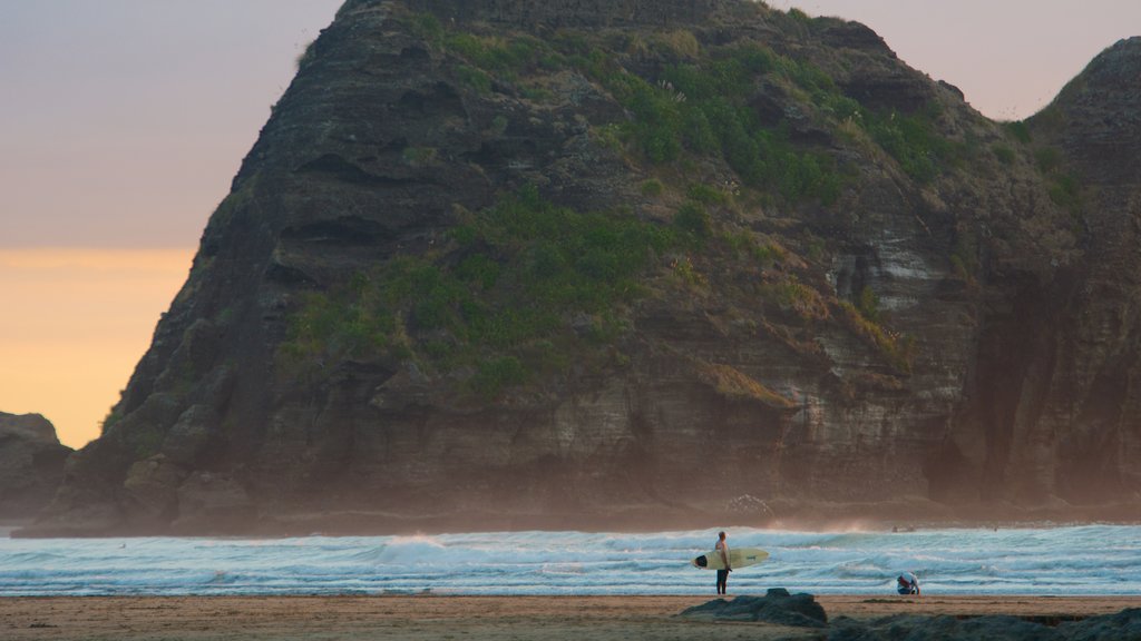 Piha Beach mostrando una playa, un atardecer y montañas