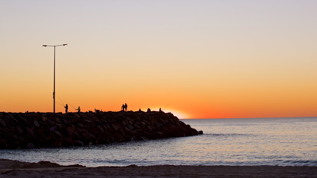 Cottesloe Beach som inkluderar en solnedgång och kustutsikter såväl som en liten grupp av människor