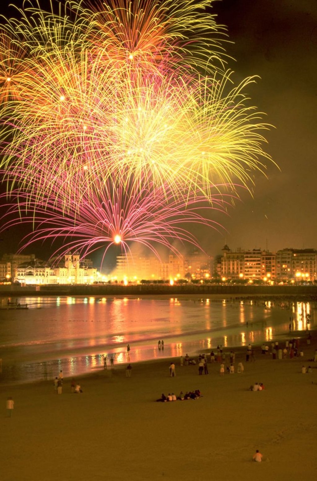 Alcuni turisti, sulla spiaggia de La Concha, a San Sebastián, guardano incantati lo spettacolo pirotecnico durante la Semana Grande. Photo credit San Sebastián Turismo