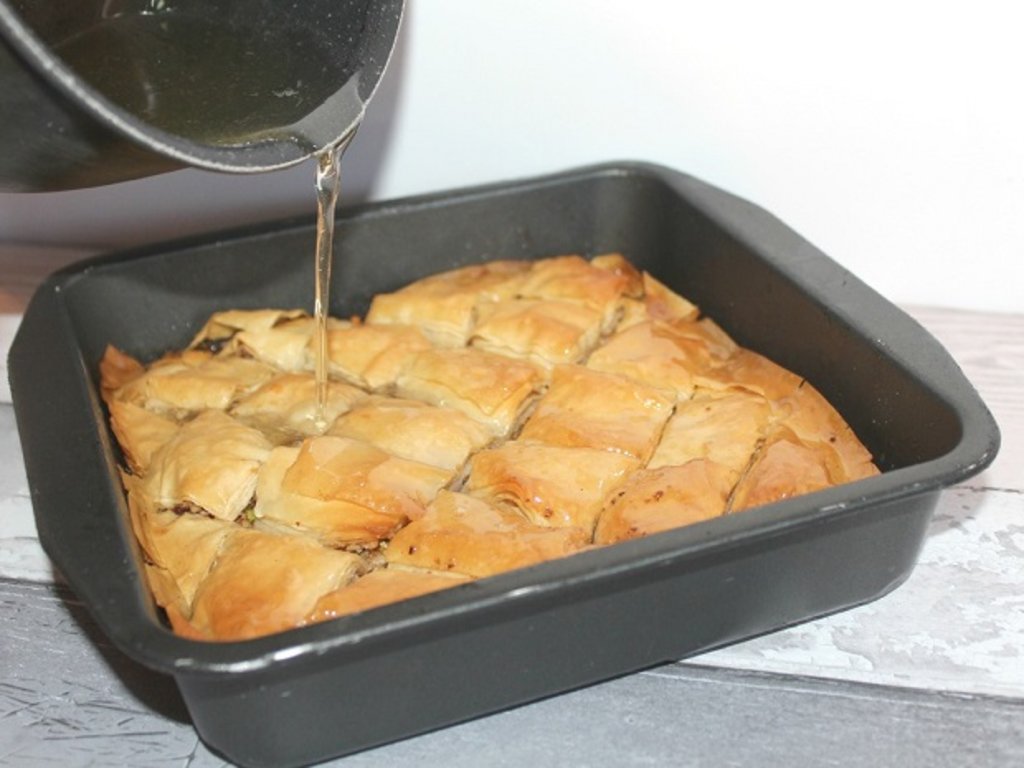 Syrup being poured over a tray of baklava