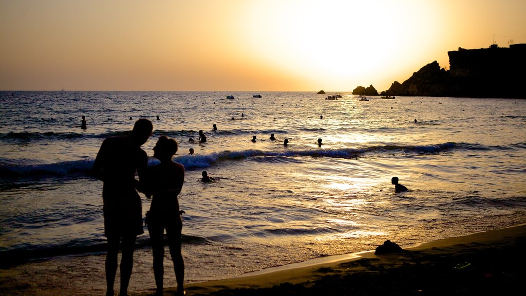 Playa de arena dorada mostrando una puesta de sol y también una pareja