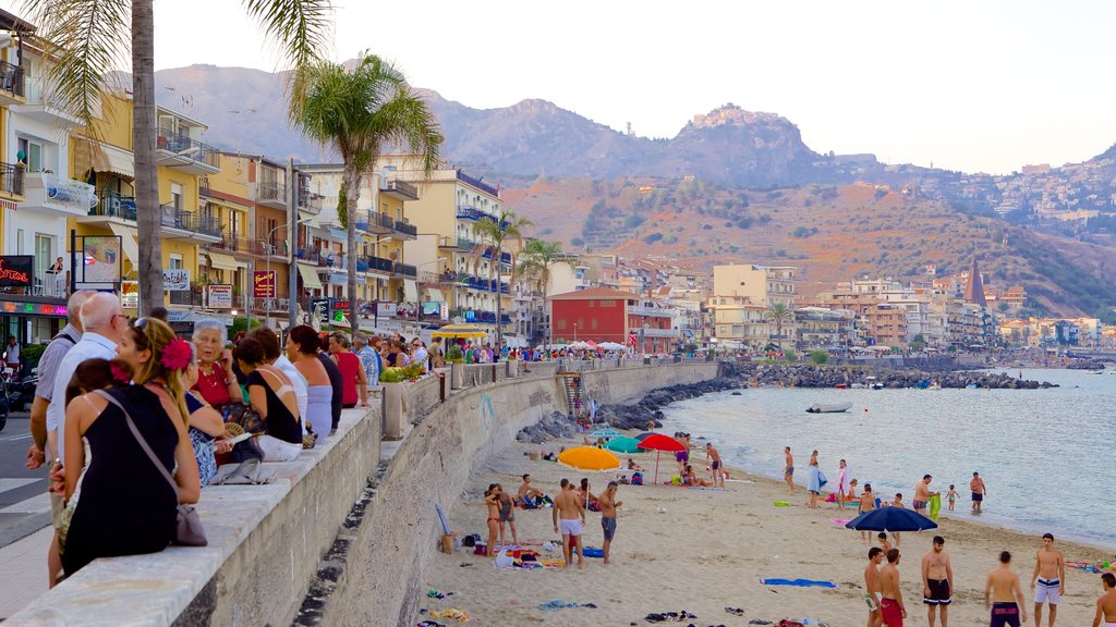 Giardini Naxos que incluye una playa de arena y una ciudad costera y también un gran grupo de personas