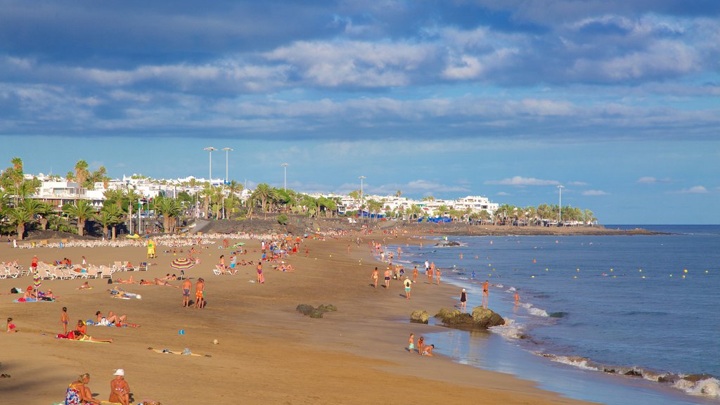 Puerto del Carmen Beach which includes a beach and general coastal views as well as a large group of people