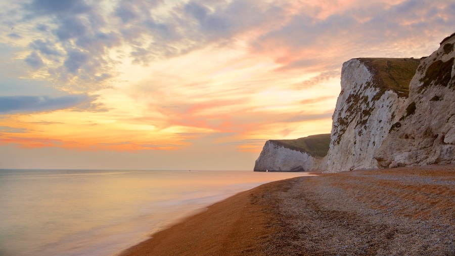 Durdle Door mostrando litoral rocoso, una playa de guijarros y un atardecer