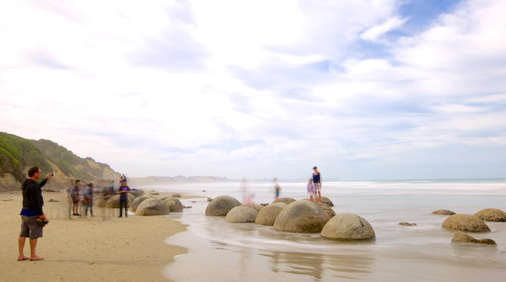 Moeraki Boulders featuring rugged coastline as well as a large group of people