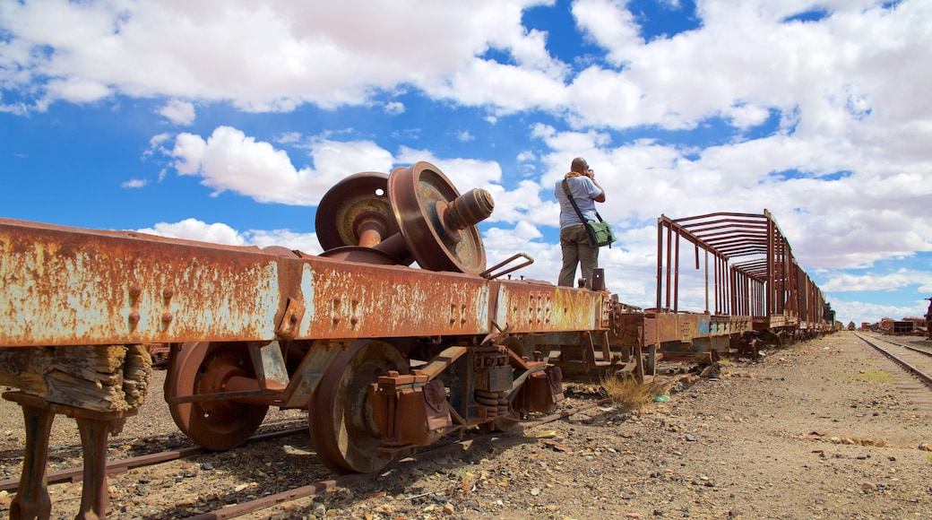 Cementerio de trenes que incluye ruinas de edificios y también un hombre