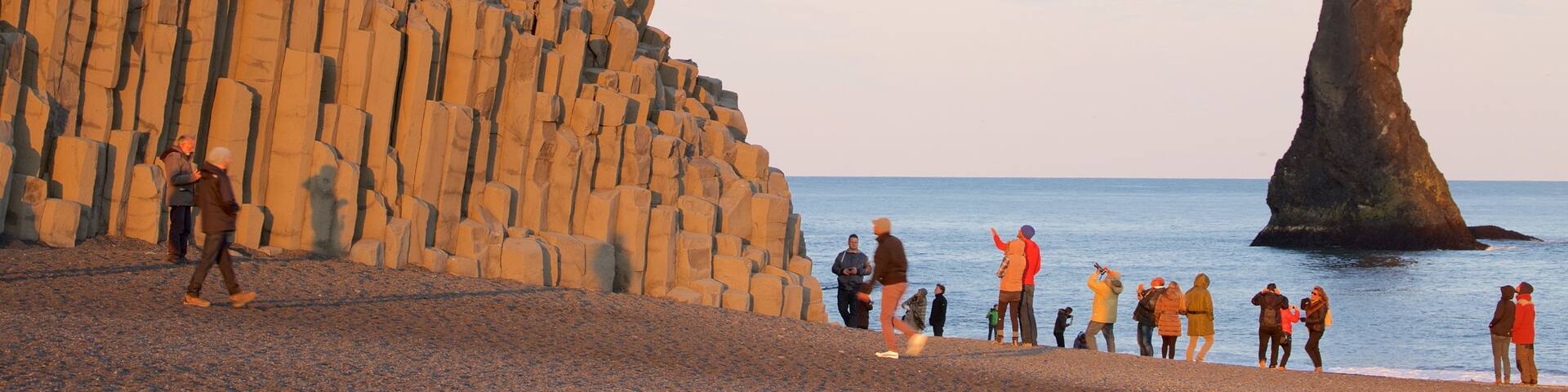 Reynisdrangar featuring general coastal views and a sunset as well as a large group of people