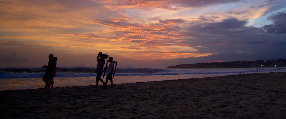 Puerto Escondido ofreciendo una puesta de sol y una playa de arena y también un pequeño grupo de personas