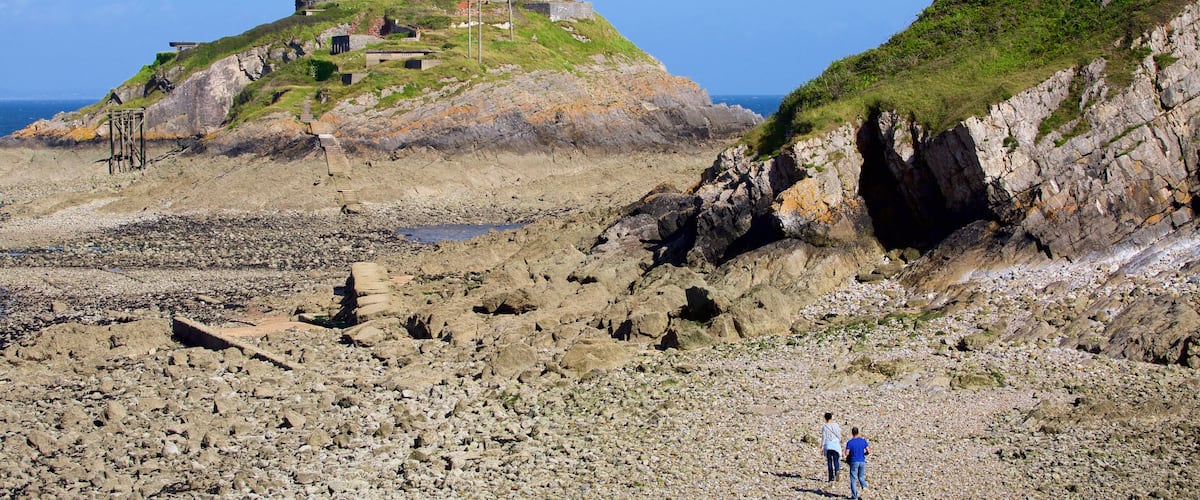 Farol de Mumbles caracterizando um farol, montanhas e uma praia de pedras