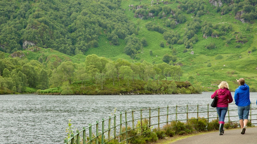 Loch Katrine featuring a lake or waterhole and forests as well as a small group of people