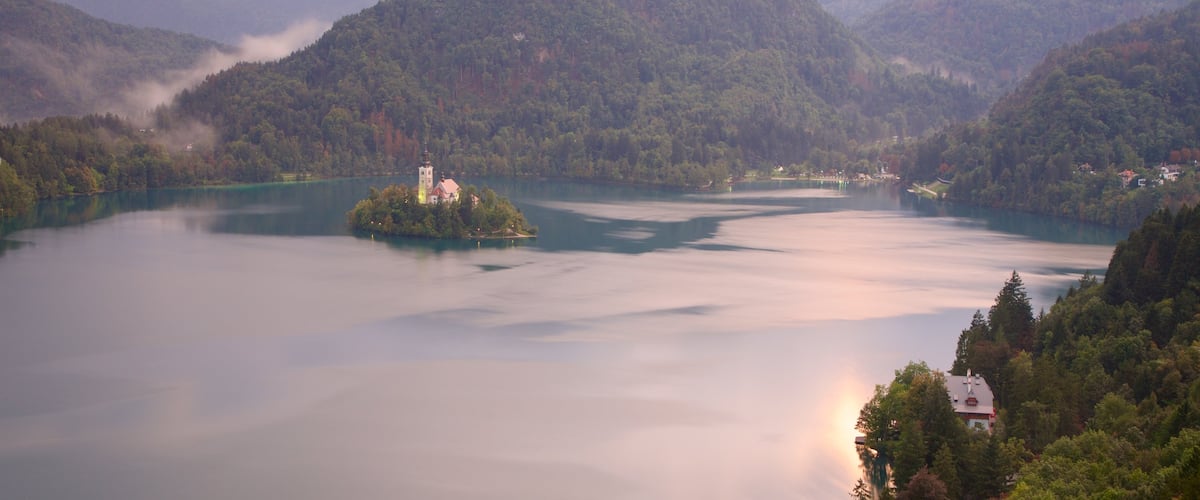 Lake Bled featuring a lake or waterhole, mist or fog and mountains
