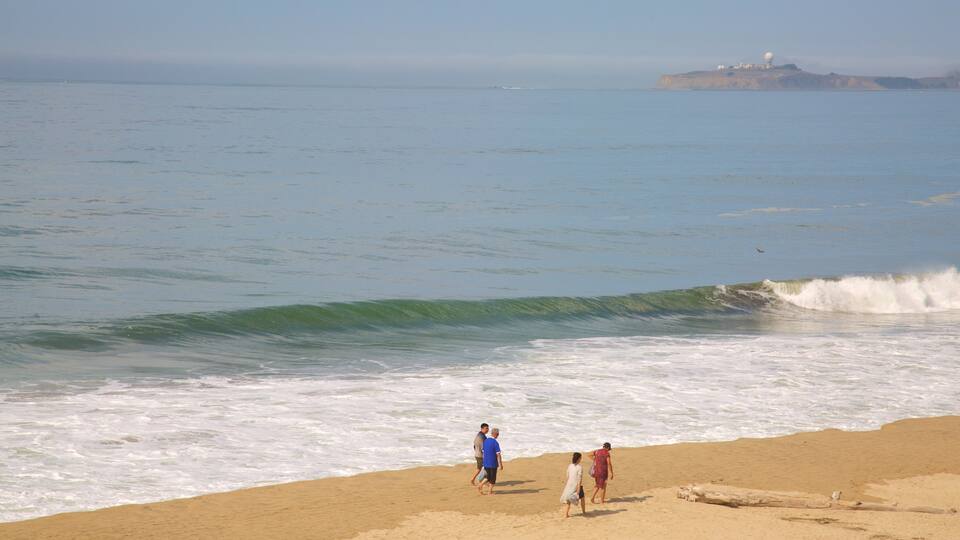 Half Moon Bay ofreciendo vistas de una costa y una playa de arena y también un grupo pequeño de personas