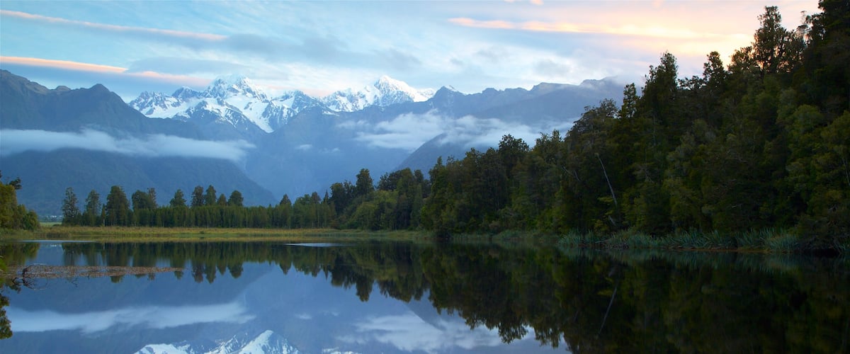 Fox Glacier som inkluderar en sjö eller ett vattenhål, en solnedgång och skogar