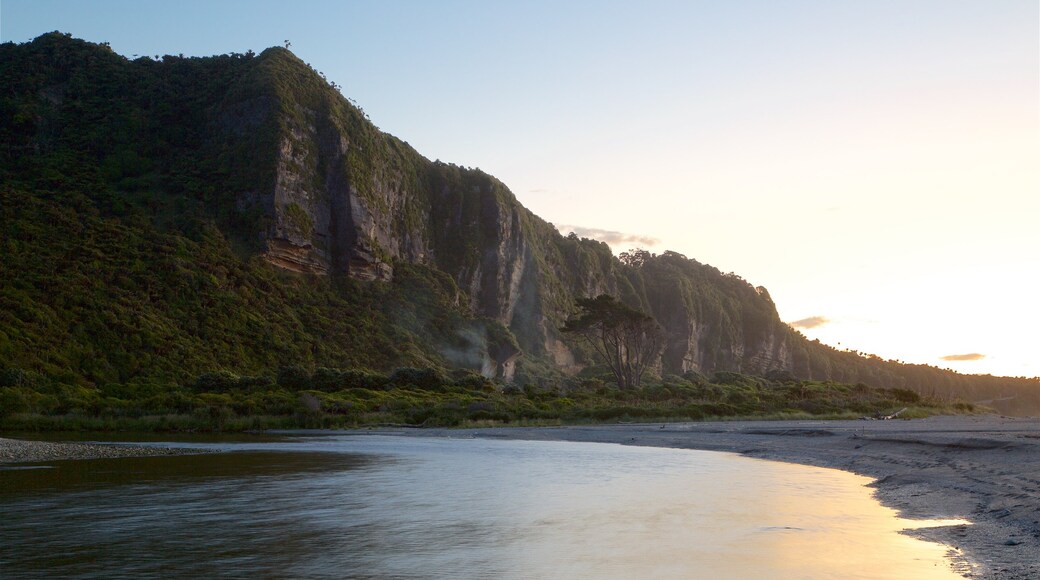 Punakaiki que incluye una puesta de sol, costa rocosa y una playa de arena