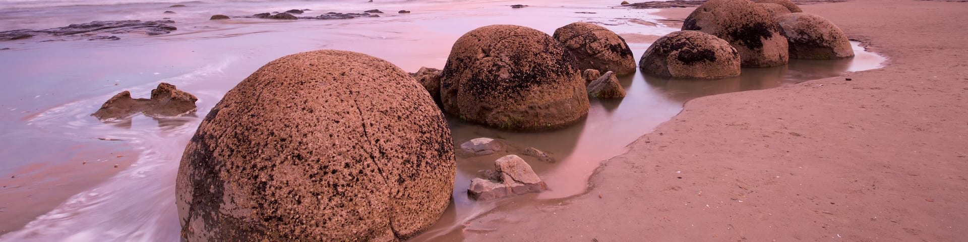 Moeraki Boulders showing rugged coastline, a sunset and a sandy beach