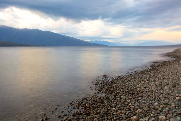 Lake Te Anau das einen Sonnenuntergang, Berge und Steinstrand