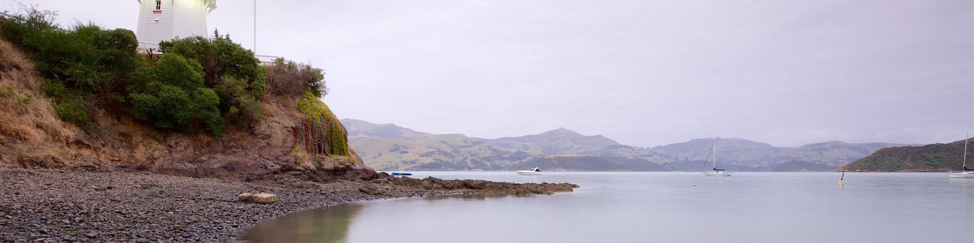 Akaroa mit einem Leuchtturm, Steinstrand und Bucht oder Hafen