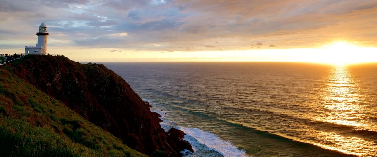 Faro de Cabo Byron que incluye una puesta de sol y costa escarpada