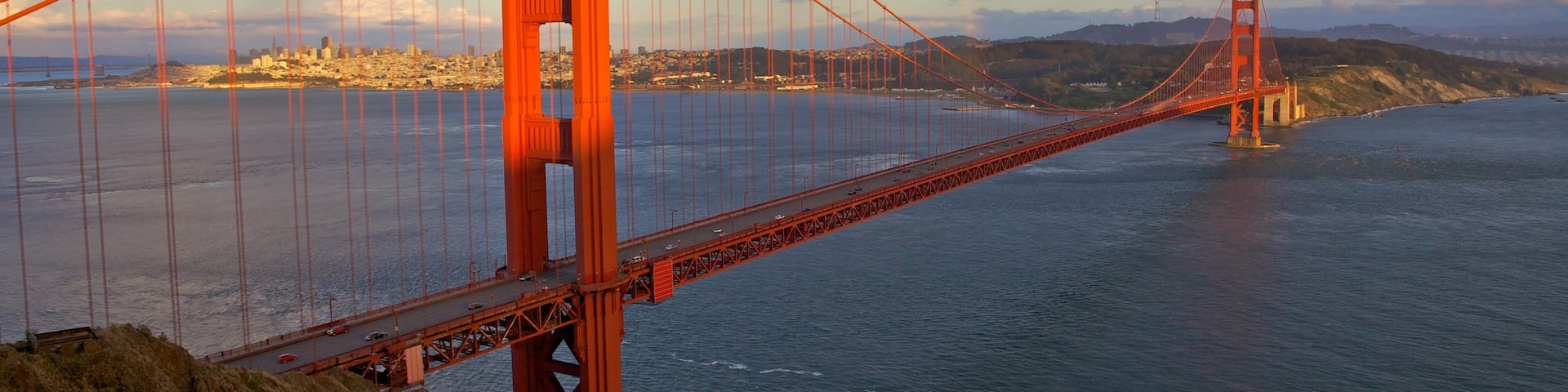 Golden Gate Bridge spans the bay in California under a dramatic sky with a hint of rainbow in the distance