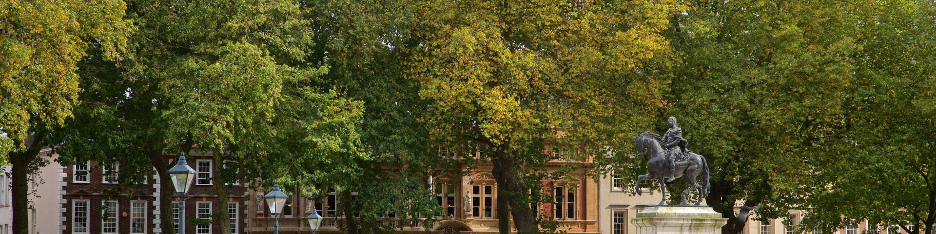 Queen Square featuring a statue or sculpture and a garden as well as a small group of people