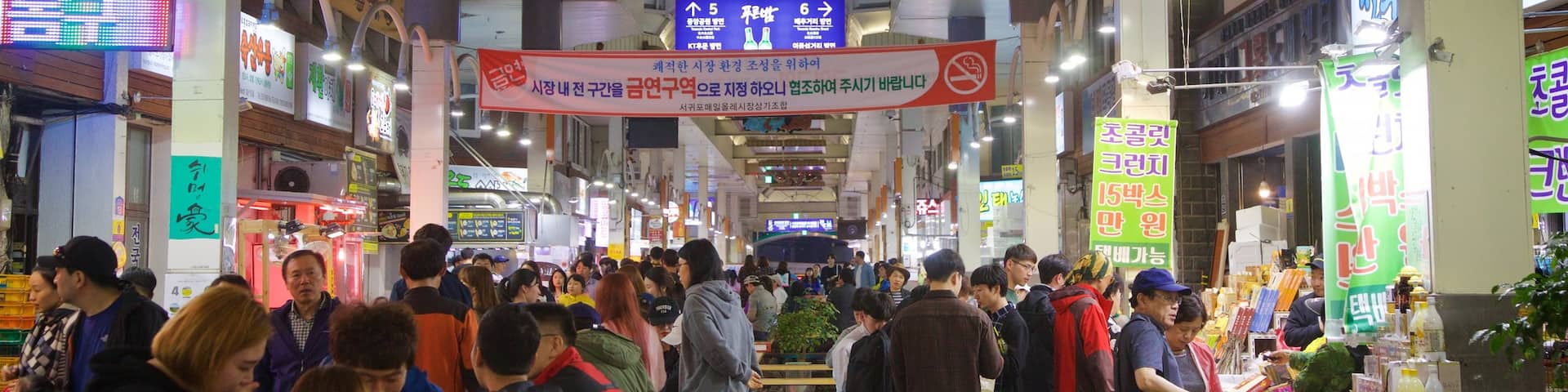 Seogwipo Maeil Olle Market showing night scenes and markets as well as a small group of people