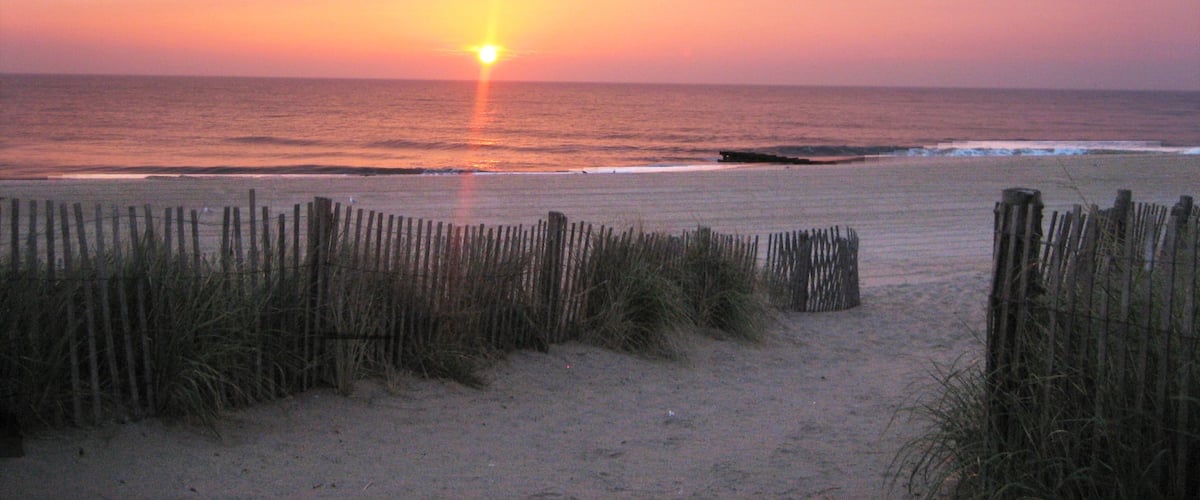 Rehoboth Beach ofreciendo una puesta de sol, una playa de arena y vistas generales de la costa