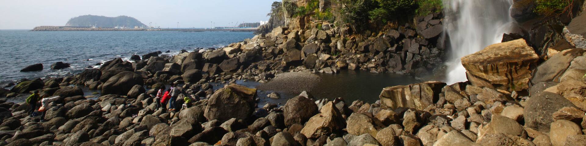 Jeongbang Waterfall featuring rocky coastline, a cascade and general coastal views