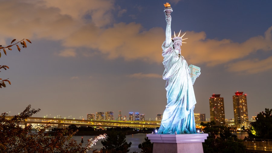 Odaiba's waterfront with a Statue of Liberty replica and illuminated cityscape in Tokyo.