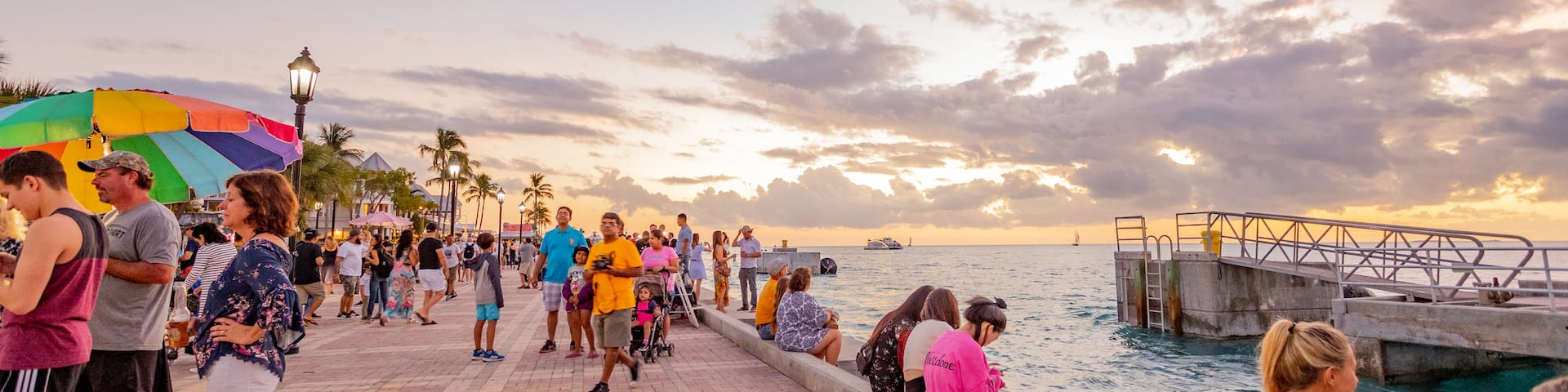 Mallory Square which includes a sunset and a bay or harbor as well as a large group of people