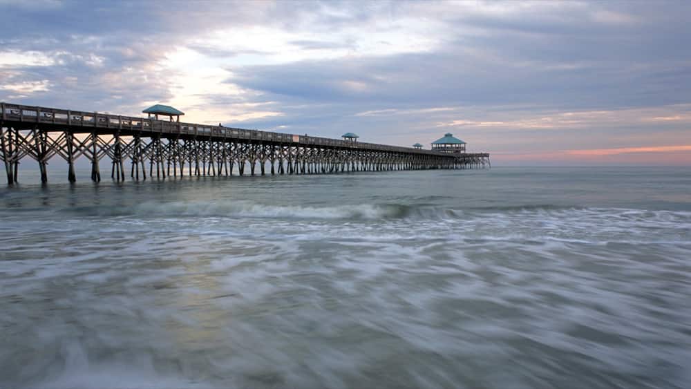 Folly Beach mit einem Sonnenuntergang, Brücke und Sandstrand