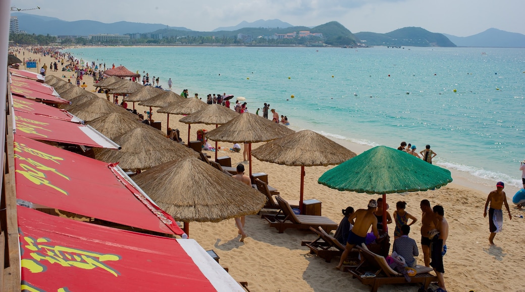 Strand von Dadonghai das einen Sandstrand und allgemeine Küstenansicht sowie große Menschengruppe