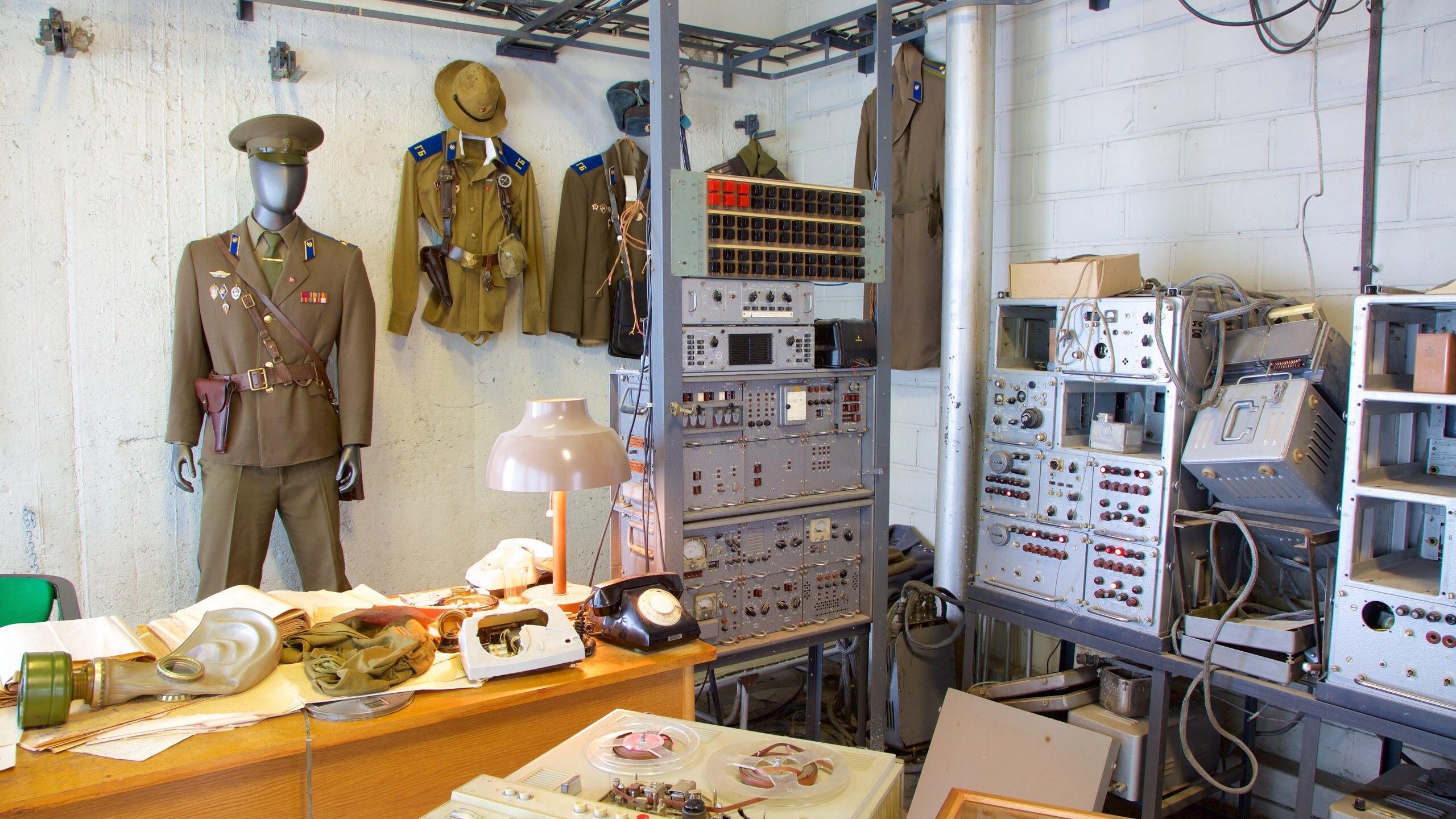 A display showcasing historical military uniforms and equipment, featuring a mannequin dressed in a military uniform with medals, surrounded by various vintage electronics and tools.