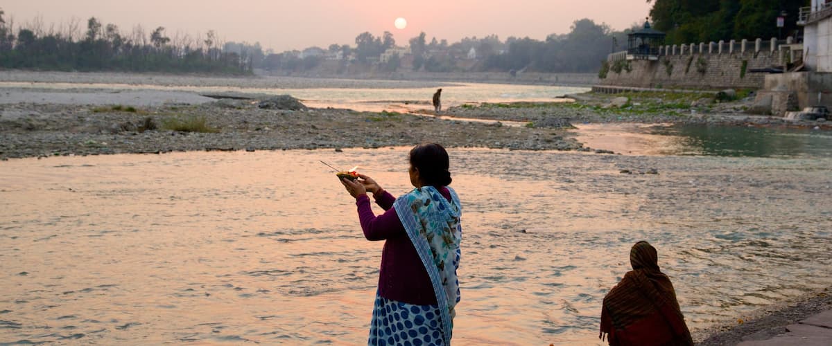 Triveni Ghat featuring a river or creek and a sunset as well as a small group of people