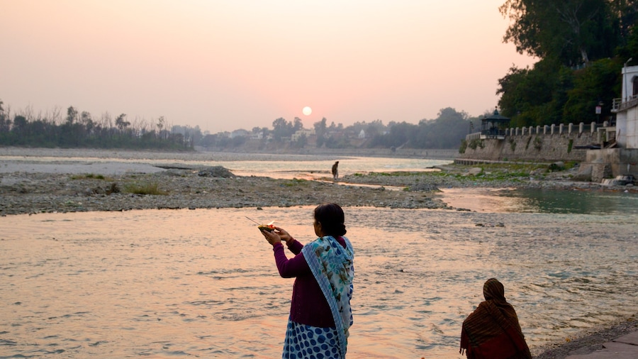 Triveni Ghat caracterizando um pôr do sol e um rio ou córrego assim como um pequeno grupo de pessoas