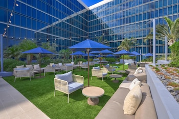 An outdoor event space with tables and chairs, a grassy lawn, and a modern building with large windows in the background.