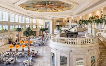 Een statige hotellobby met een vleugelpiano, verschillende eetgedeeltes en een fontein in het midden.