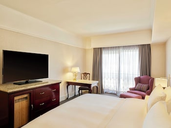 Habitación de hotel con dos camas, una mesita de noche con teléfono, lámparas y una silla junto a la ventana.