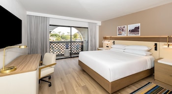 A hotel room with a bed, desk, chair, and a balcony with a view.