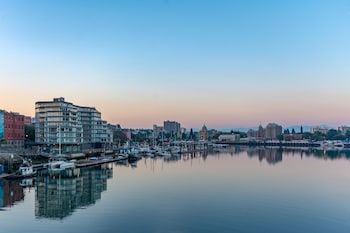 Un puerto deportivo con barcos amarrados, un horizonte urbano al fondo y una vista desde un balcón con mesa y sillas.